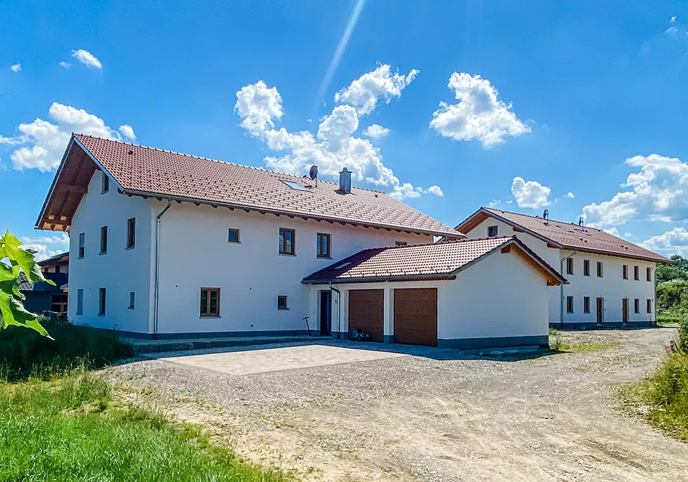 Zwei moderne Wohnhäuser mit rotem Satteldach, Garage im Vordergrund, unter blauem Himmel mit wenigen Wolken.