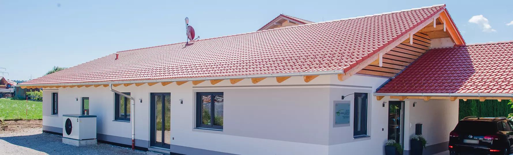 Hauseingang mit Glas­tür unter einem großen Holzvordach, flankiert von zwei Pflanzkübeln und beleuchtet mit Wandlampen.