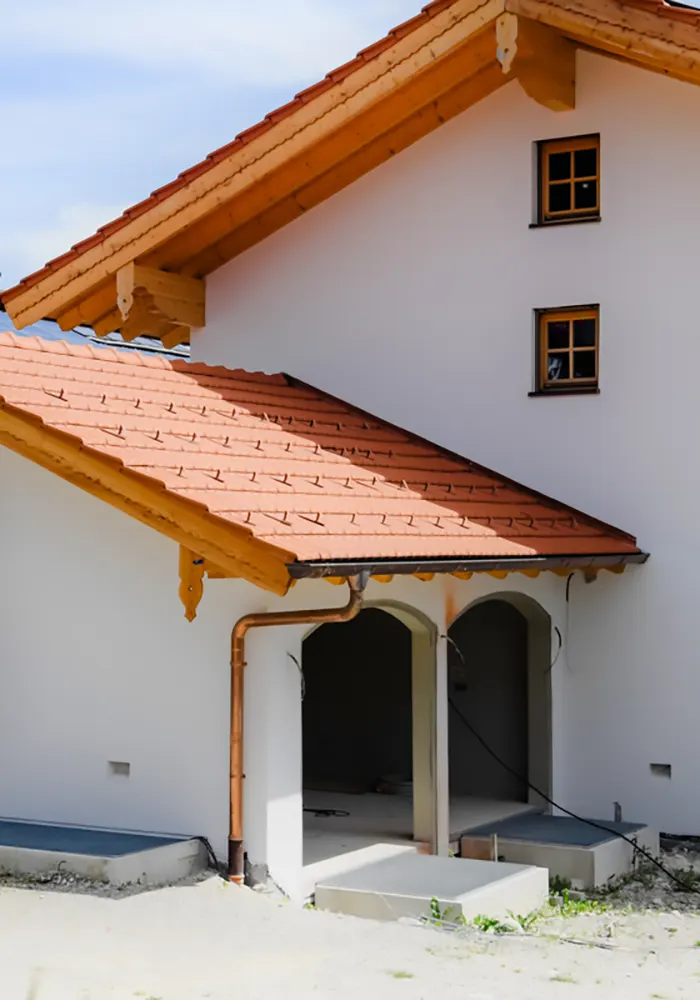 Detailaufnahme eines Hauseingangs mit roten Ziegeldächern, Rundbogen und Kupferregenrinne.