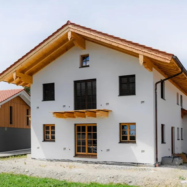 Zweistöckiges Haus mit Holzgiebel, weißen Wänden und Rollläden, Baustelle im Eingangsbereich.