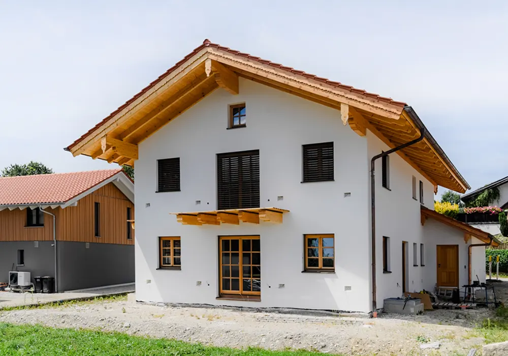 Zweistöckiges Haus mit Holzgiebel, weißen Wänden und Rollläden, Baustelle im Eingangsbereich.