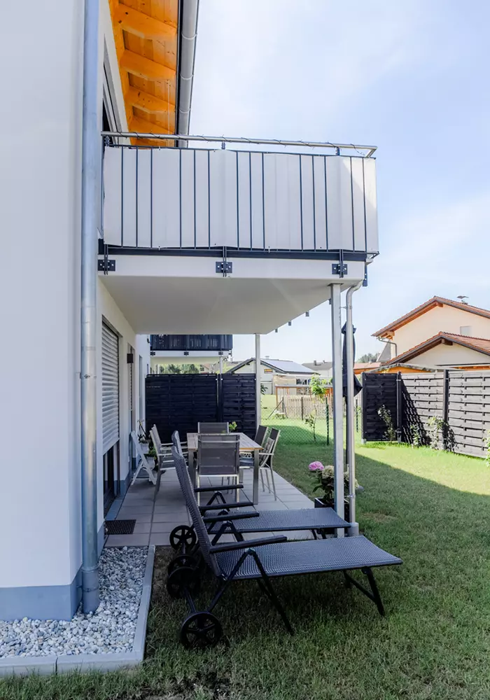 Überdachte Terrasse mit Tisch, Stühlen und zwei Sonnenliegen im Garten eines modernen Einfamilienhauses.