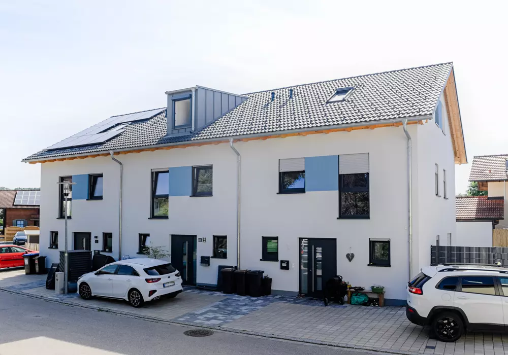 Modernes Doppelhaus mit Solarpanels, parkenden Autos und kleinem Vorgarten an einer ruhigen Wohnstraße.