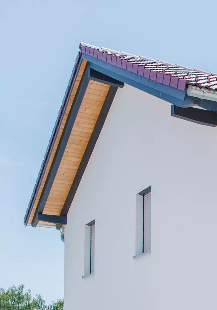 Nahaufnahme eines Giebels mit weißer Fassade, Holzuntersicht und roten Dachziegeln.