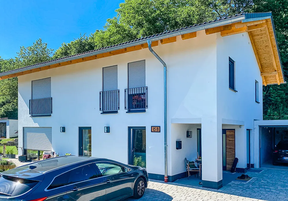Modernes weißes Wohnhaus mit Carport, geparktem Auto und möblierter Eingangsbereich auf gepflastertem Hof.