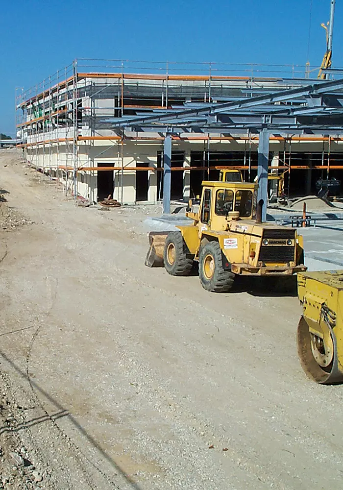 Große Baustelle mit Gerüst, Stahlträgern und Baumaschinen vor einem mehrstöckigen Rohbau.