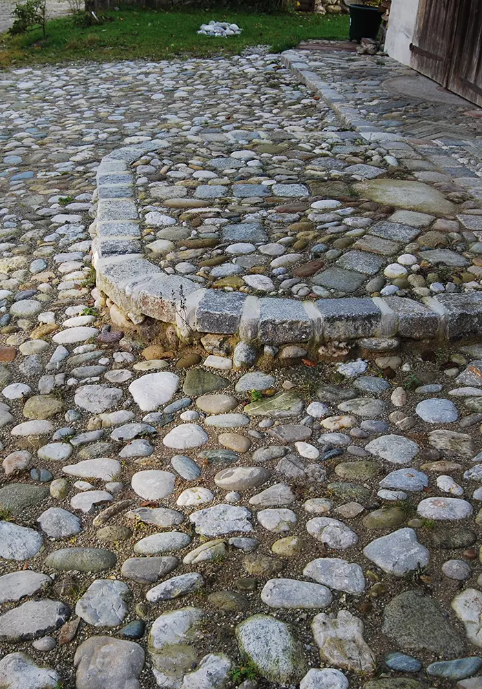 Historischer gepflasterter Hof mit runden Flusssteinen und erhöhtem Stufenbereich aus Naturstein.