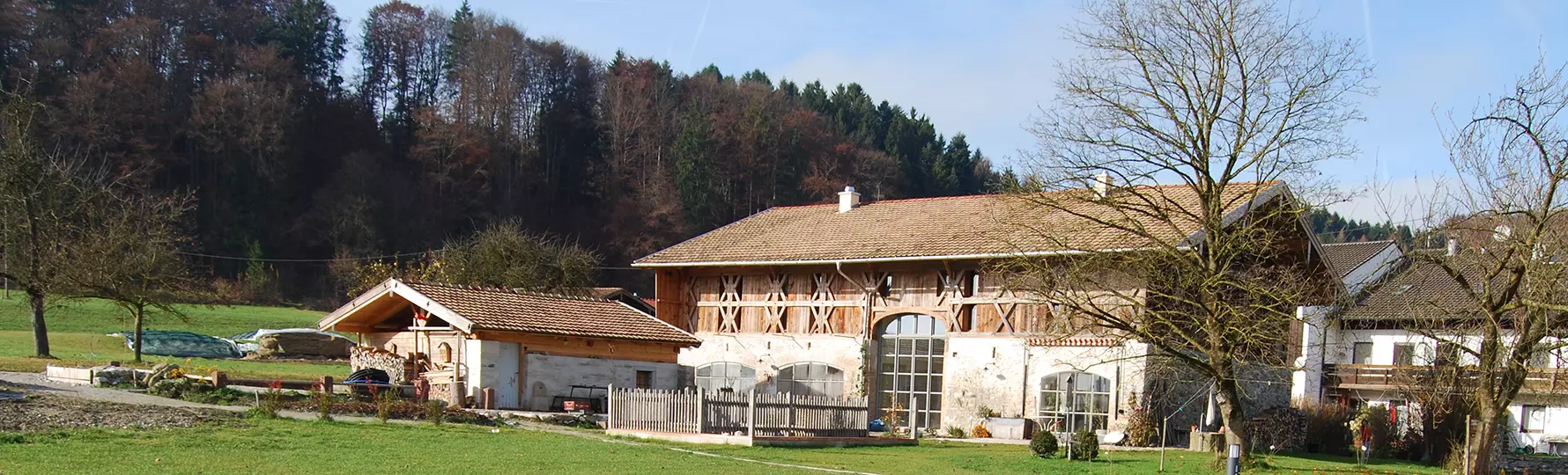 Großer, restaurierter Hof mit Holzfassade, Nebengebäuden und Garten, umgeben von Wiesen und Bäumen am Waldrand.