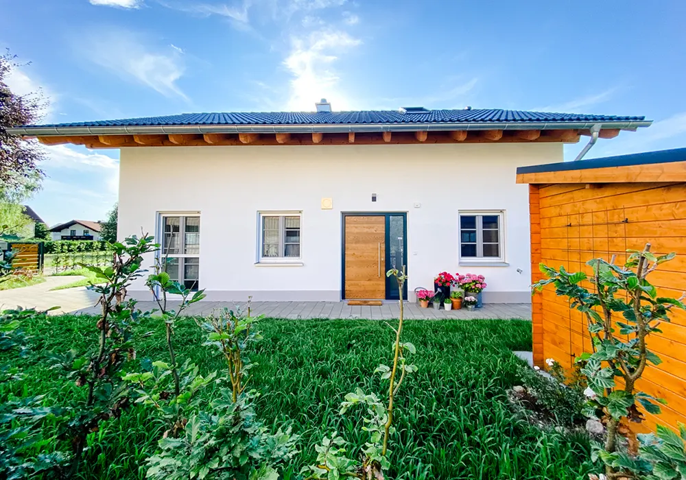 Weißes Einfamilienhaus mit Holztür, Vorgarten und Blumentöpfen, bei sonnigem Wetter fotografiert.