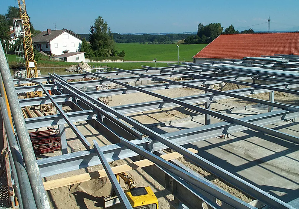 Stahlkonstruktion eines Neubaus auf Baustelle mit Kran, Bagger und umliegender Landschaft.