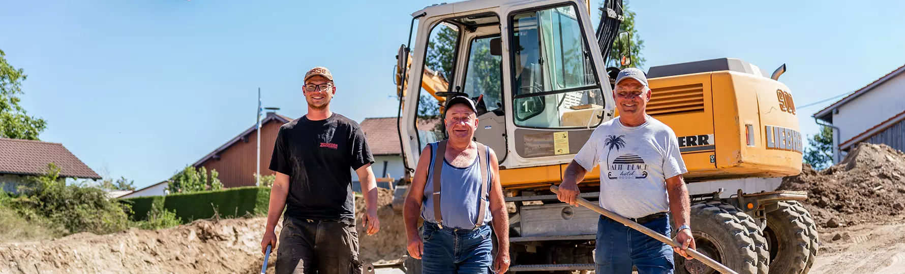 Drei Bauarbeiter gehen lächelnd über die Baustelle, im Hintergrund ein Bagger.