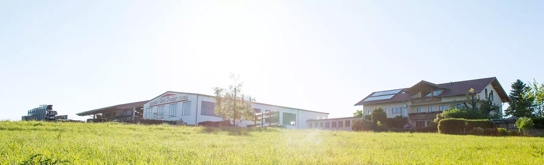 Firmengebäude von „Seb. Pauker Hochbau Tiefbau“ und benachbartes Wohnhaus mit Solaranlage auf einem sonnigen Wiesengrundstück.