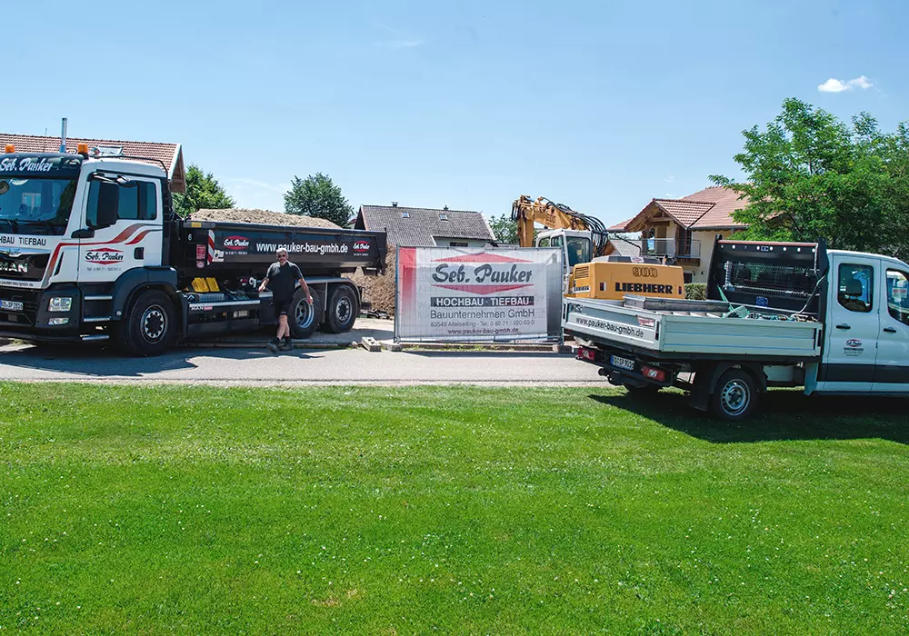 Bauunternehmen-Fahrzeuge und Bagger vor Bauzaun mit Banner von Seb. Pauker Hochbau Tiefbau GmbH.