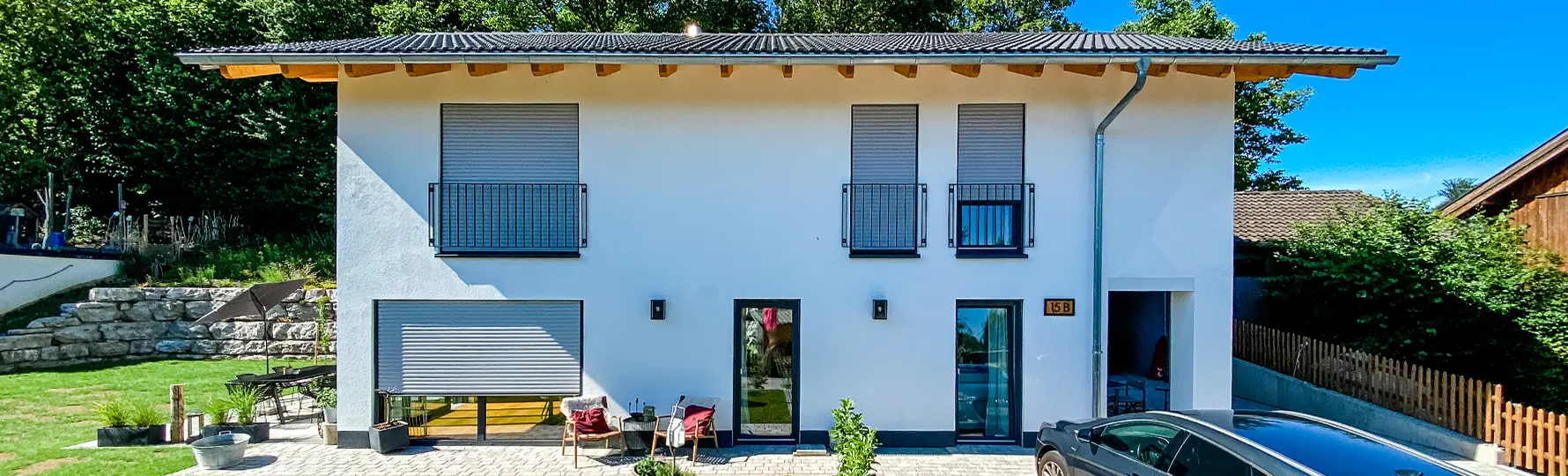 Modernes, zweistöckiges Einfamilienhaus mit Flachdach, geschlossenen Rollläden und kleinem Vorgarten mit Sitzgruppe.