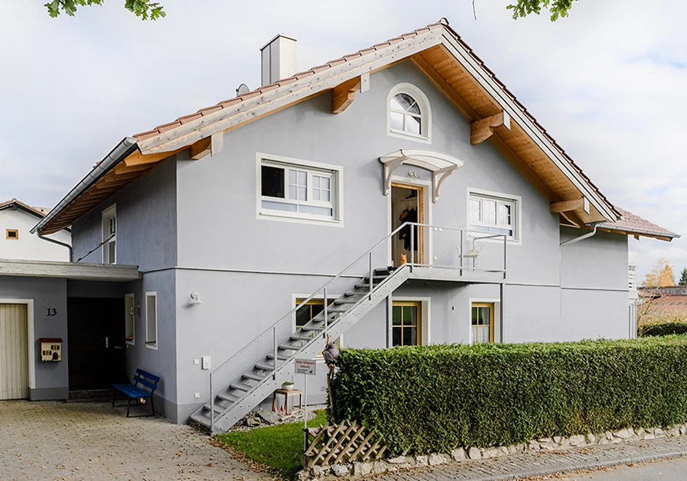 Frontansicht eines aufgestockten Hauses mit Außentreppe, neuen Fenstern und Vorgartenhecke