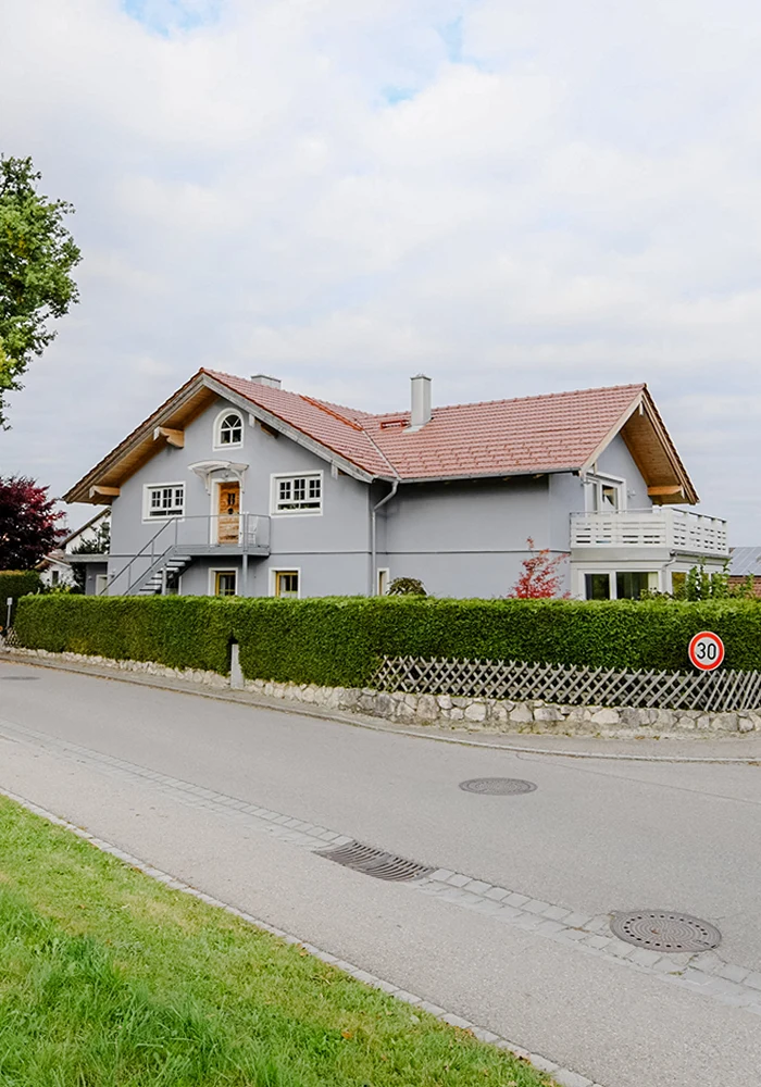 Straßenansicht eines modernisierten Wohnhauses mit Aufstockung, Balkon und großer Dachfläche