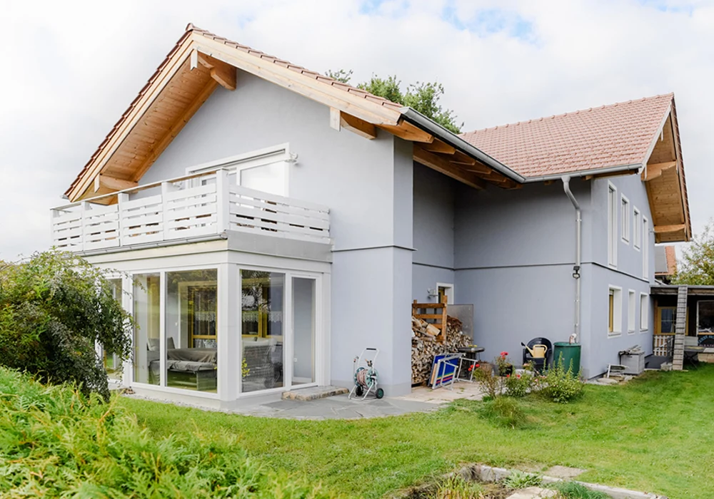 Rückseite eines Hauses mit Balkon, großen Fensterflächen und Garten