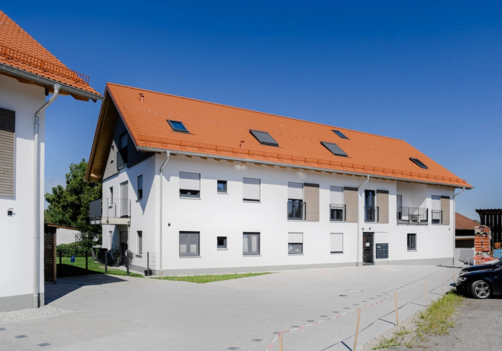 Mehrfamilienhaus mit Ziegeldach und gepflasterter Hoffläche vor dem Gebäude