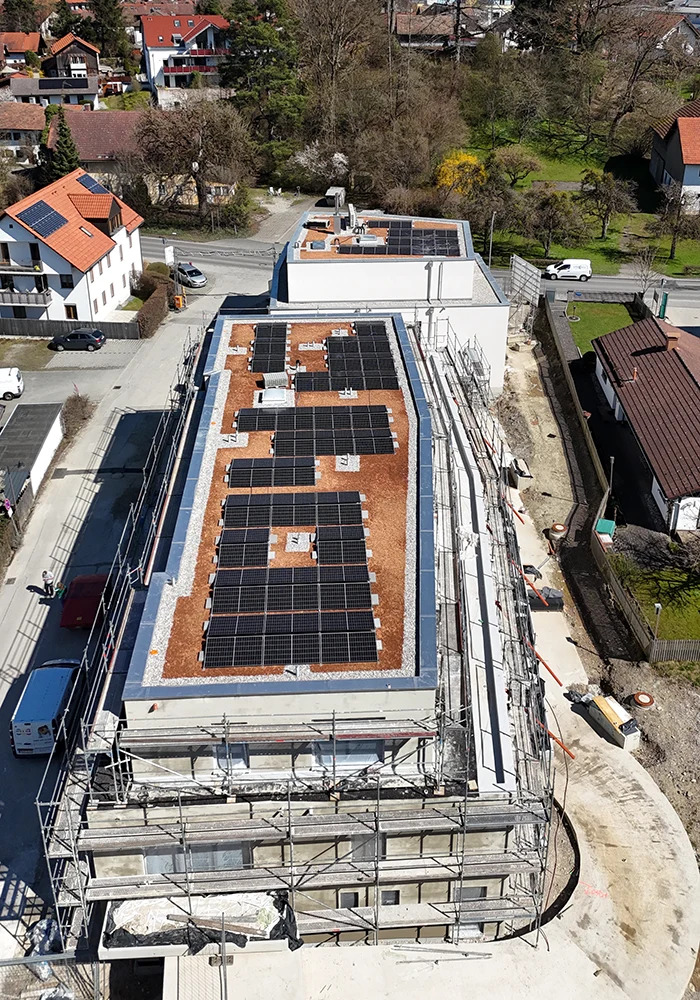 Drohnenaufnahme eines Flachdachgebäudes mit Solaranlagen auf Kiesdach, Fassade im Bau, Gerüste rund ums Haus.