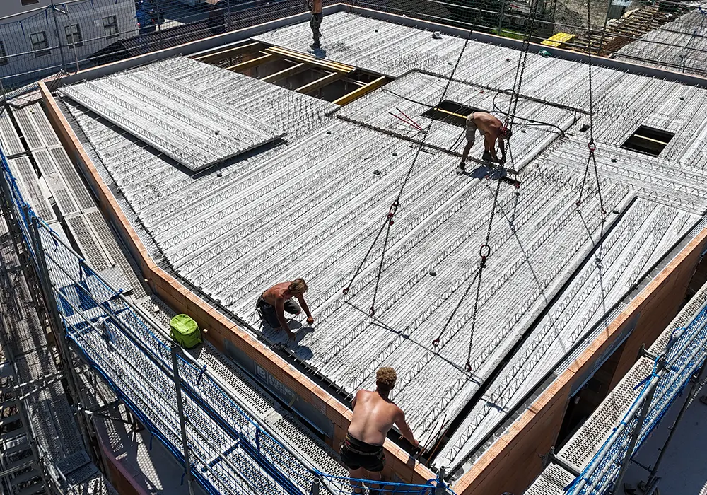 Mehrere Bauarbeiter montieren vorgefertigte Betondeckenelemente mit Stahlbewehrung auf einem Neubau.