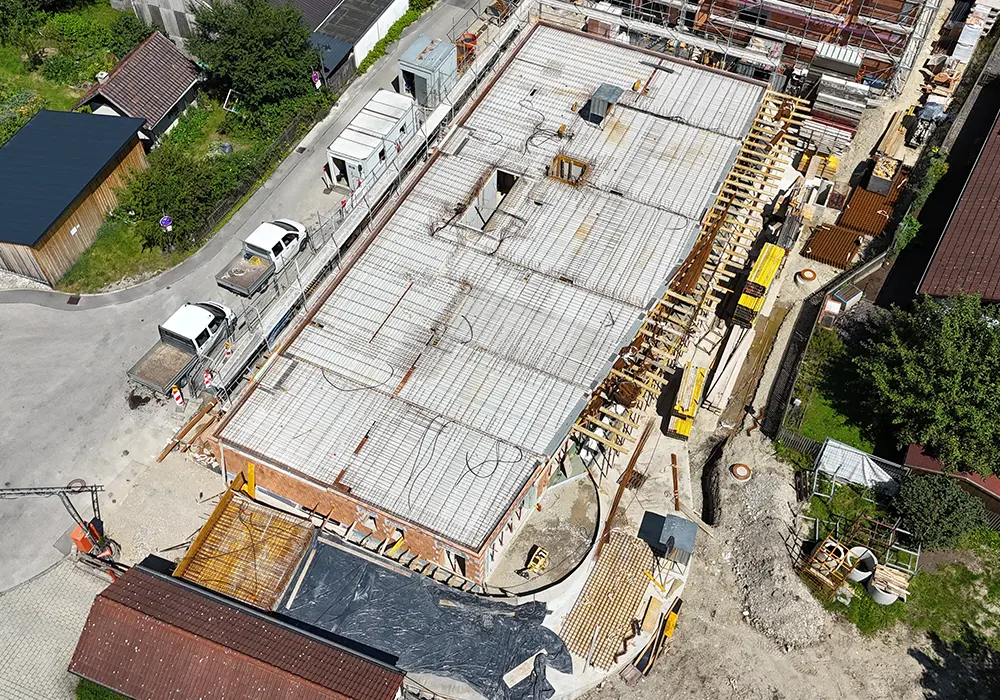 Luftaufnahme eines Rohbaus mit fertig verlegter Bewehrung für Betondecke, umliegende Baustelle mit Baumaterialien.