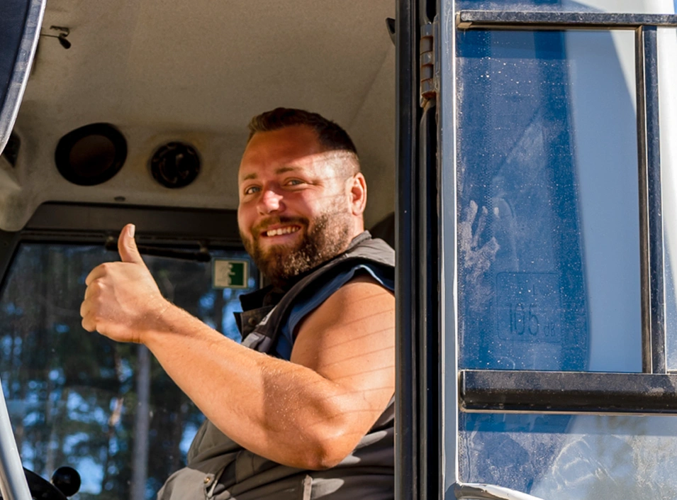 Lächelnder Bauarbeiter zeigt Daumen hoch in der Fahrerkabine einer Baumaschine.