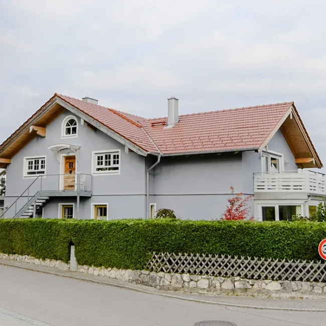 Mehrgenerationenhaus mit Balkon, großem Dach und Hecke entlang der ruhigen Wohnstraße
