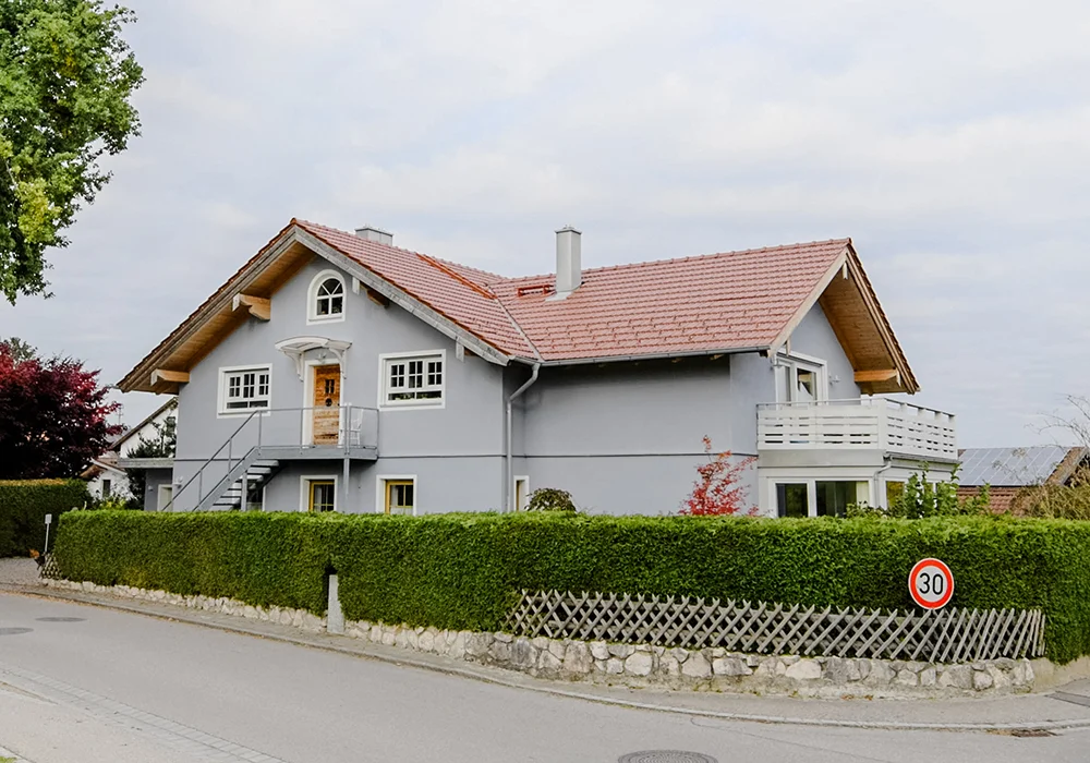 Mehrgenerationenhaus mit Balkon, großem Dach und Hecke entlang der ruhigen Wohnstraße