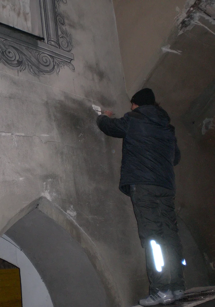 Arbeiter entfernt beschädigten Putz an der Wand des Torbogens bei Sanierungsarbeiten