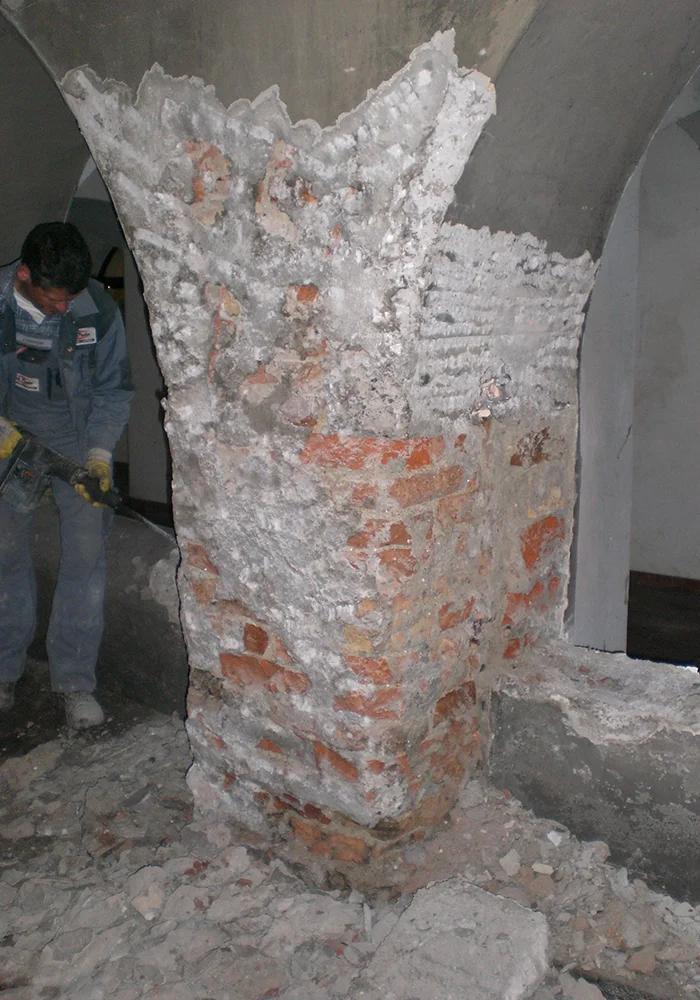 Arbeiter stemmt alten Putz von einem massiven Mauerpfeiler im Torbogenbereich ab