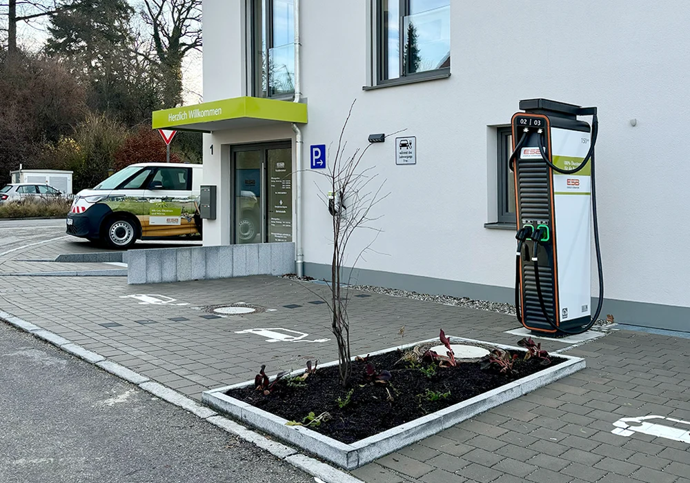 E-Ladestation vor einem Bürogebäude mit Stellplätzen und Eingangsbereich