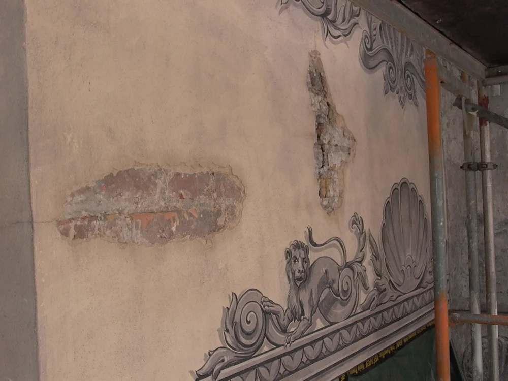 Historische Fassadenmalerei mit freigelegten Putzschäden während Restaurierungsarbeiten
