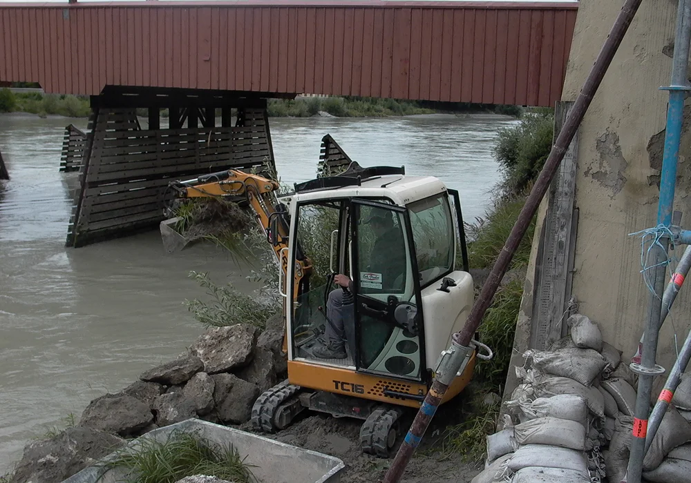Bagger entfernt Sand und Geröll am Ufer des Inns neben Brückenkonstruktion