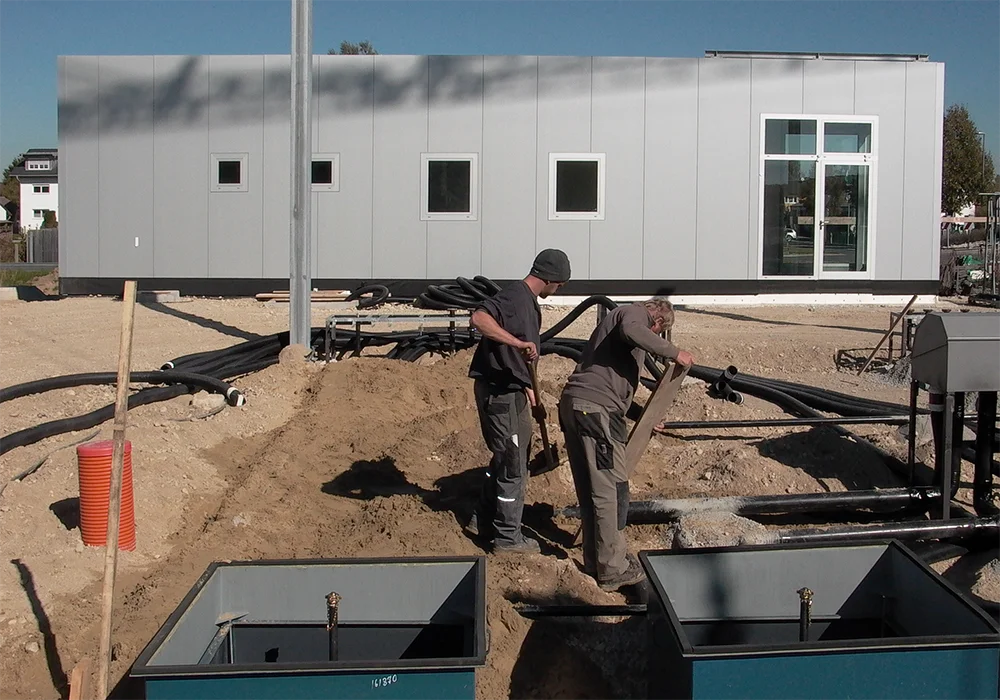 Arbeiter verlegen Leitungen im Sandbett vor Gewerbebau mit vorbereiteten Schächten