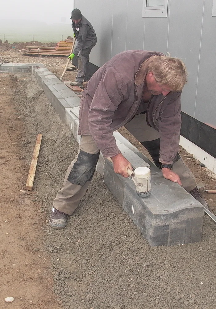 Arbeiter setzt Steine mit Gummihammer entlang des Gebäudes