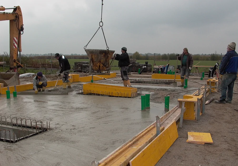 Bauarbeiter verteilen frischen Beton für Bodenplatte zwischen Schalung und Bewehrung