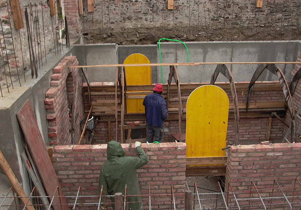 Bauarbeiter errichten gemauerte Gewölbewände im neuen Keller innerhalb eines Bestandsgebäudes