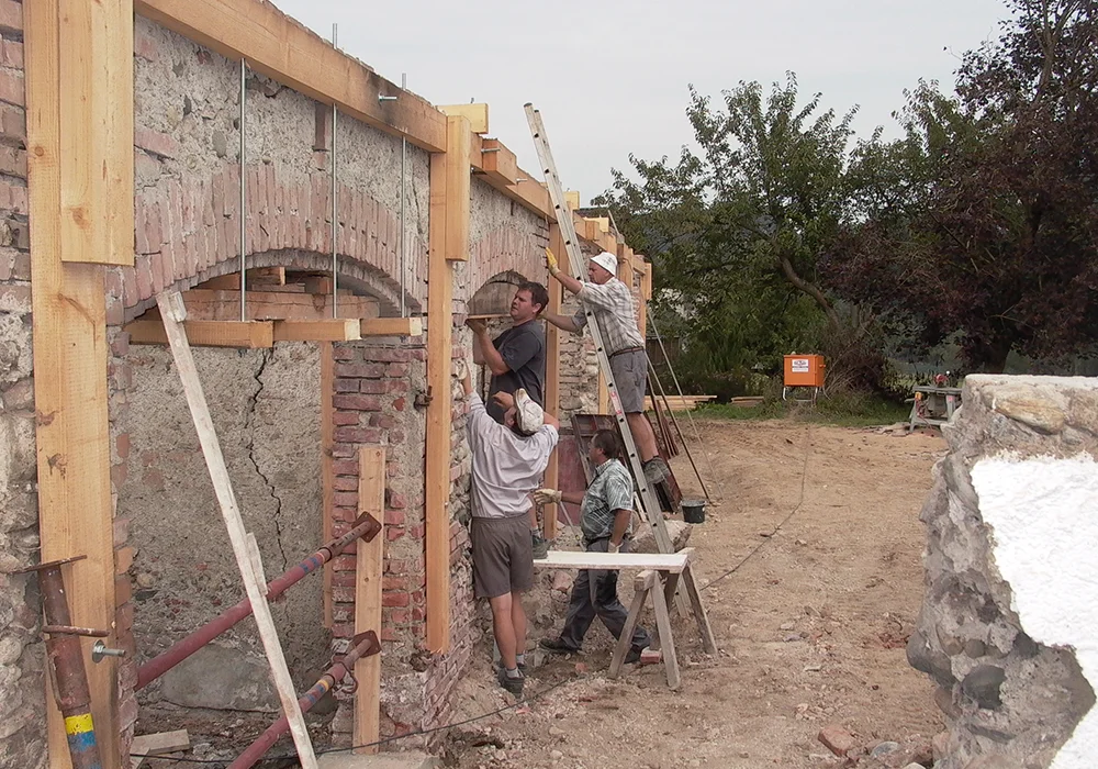 Handwerker sichern alte Steinwand mit Holzkonstruktion und Abstützungen auf einem Bauernhof