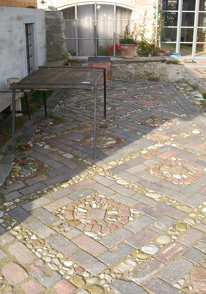 Gepflasterter Innenhof mit Natursteinmauer, Tisch und großem Gewölbefenster