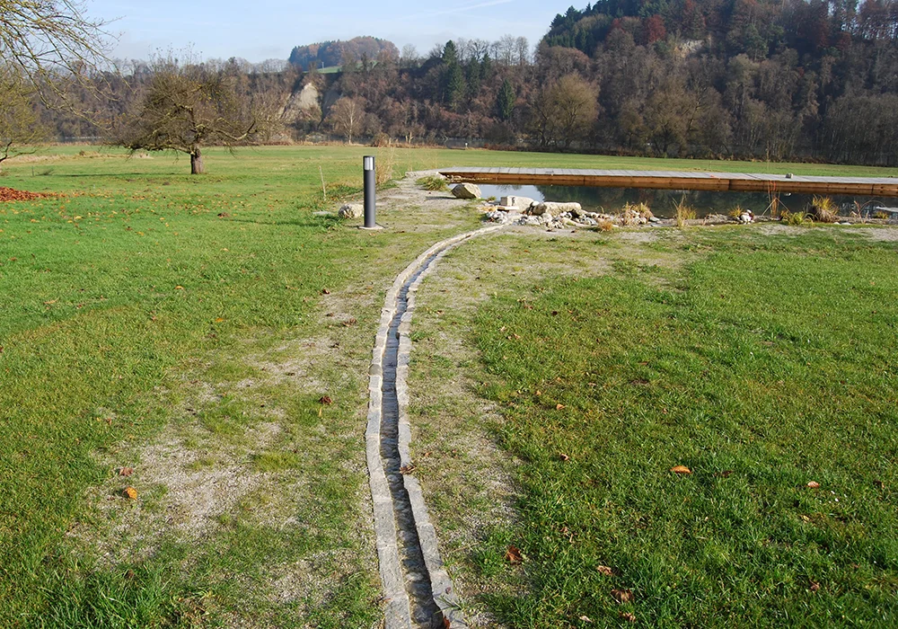 Geschwungener Pflasterweg, Zulauf führt über die Wiese zu Teich und Liegefläche