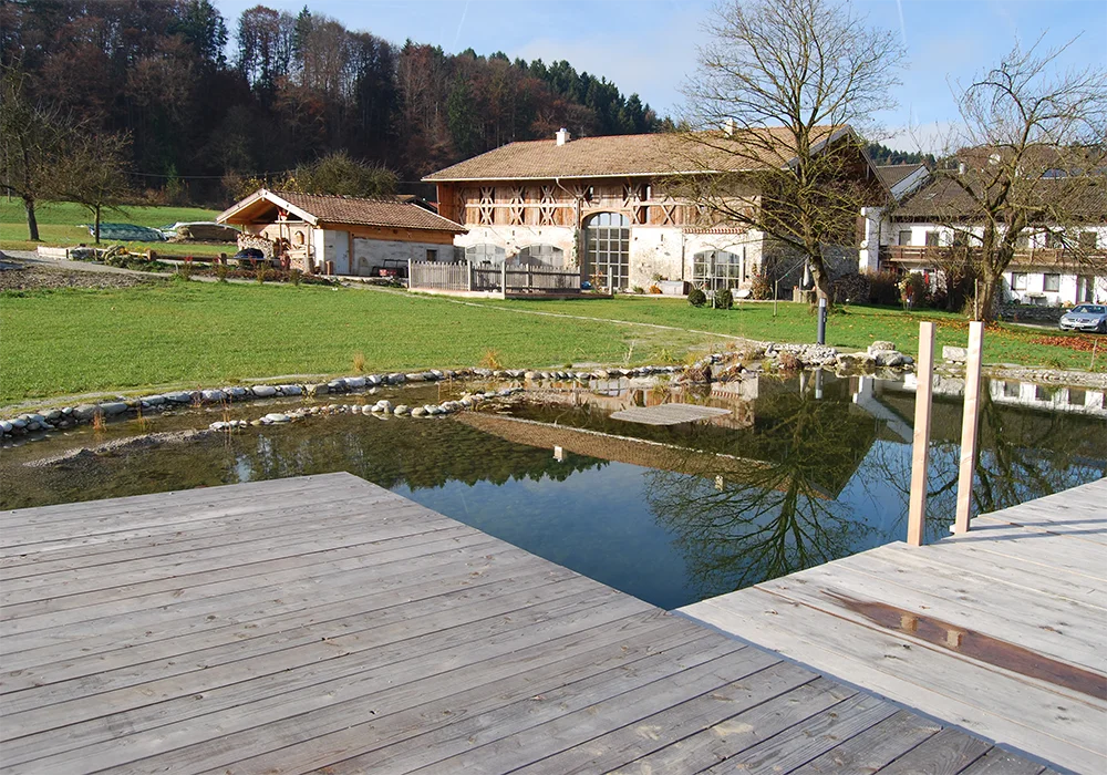 Blick über Schwimmteich zu einem sanierten Bauernhof in ländlicher Umgebung