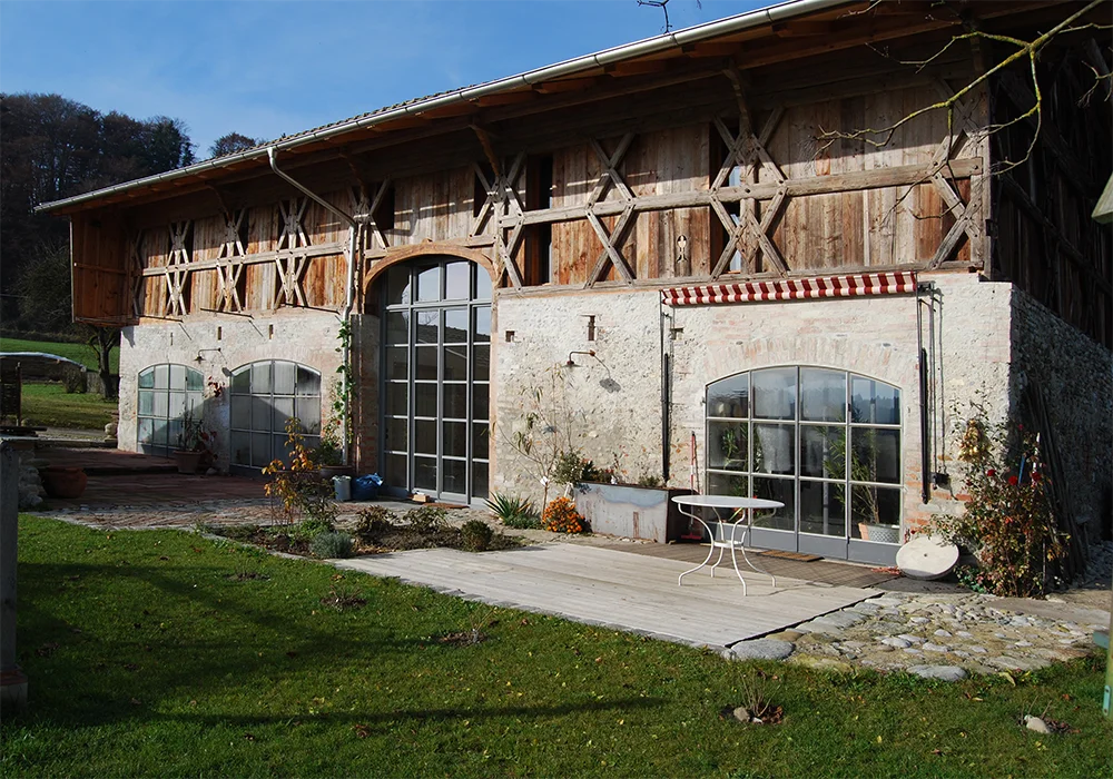 Rückseite eines sanierten Bauernhofs mit großer Glasfront, Terrasse und Gartenfläche