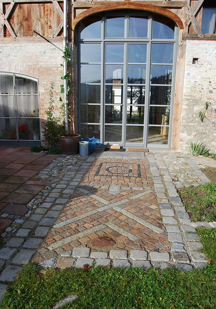 Eingangsbereich mit dekorativem Pflastermuster vor hoher Glasfront im Gewölbebereich