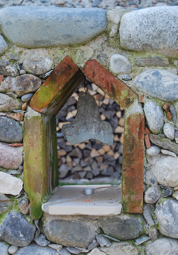 Kleine Nische aus Natursteinmauerwerk mit Steinglocke und gemauertem Spitzbogen