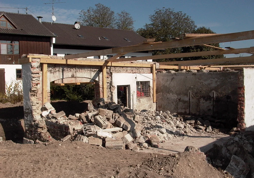 Freigelegtes Bestandsgebäude eines Bauernhofs mit Schutt, Holzbalken und offenen Steinwänden während des Umbaus